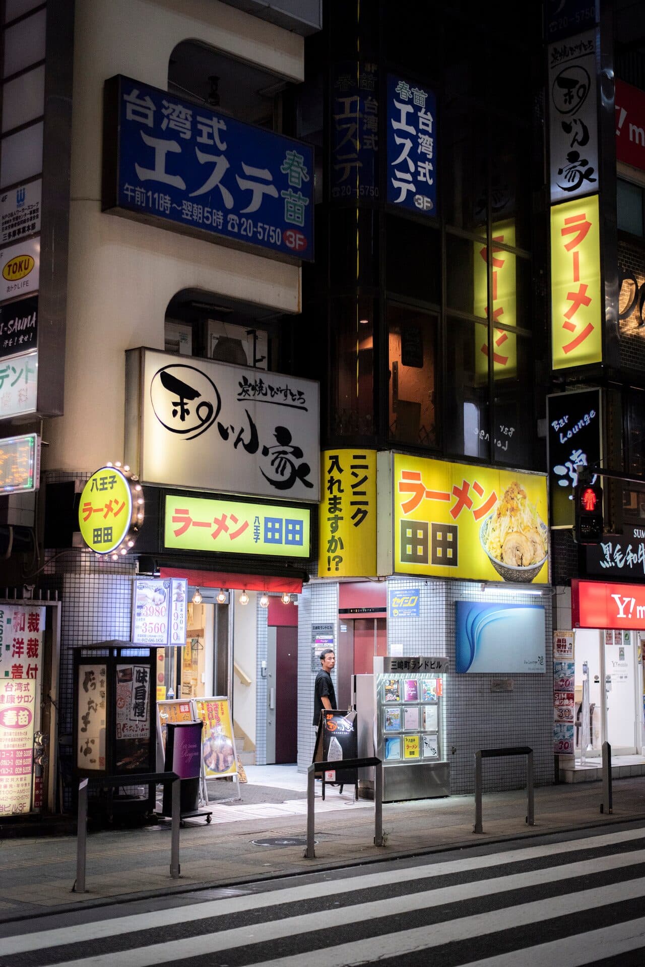 Glowing ramen shop signs on a Hachioji street corner at night
